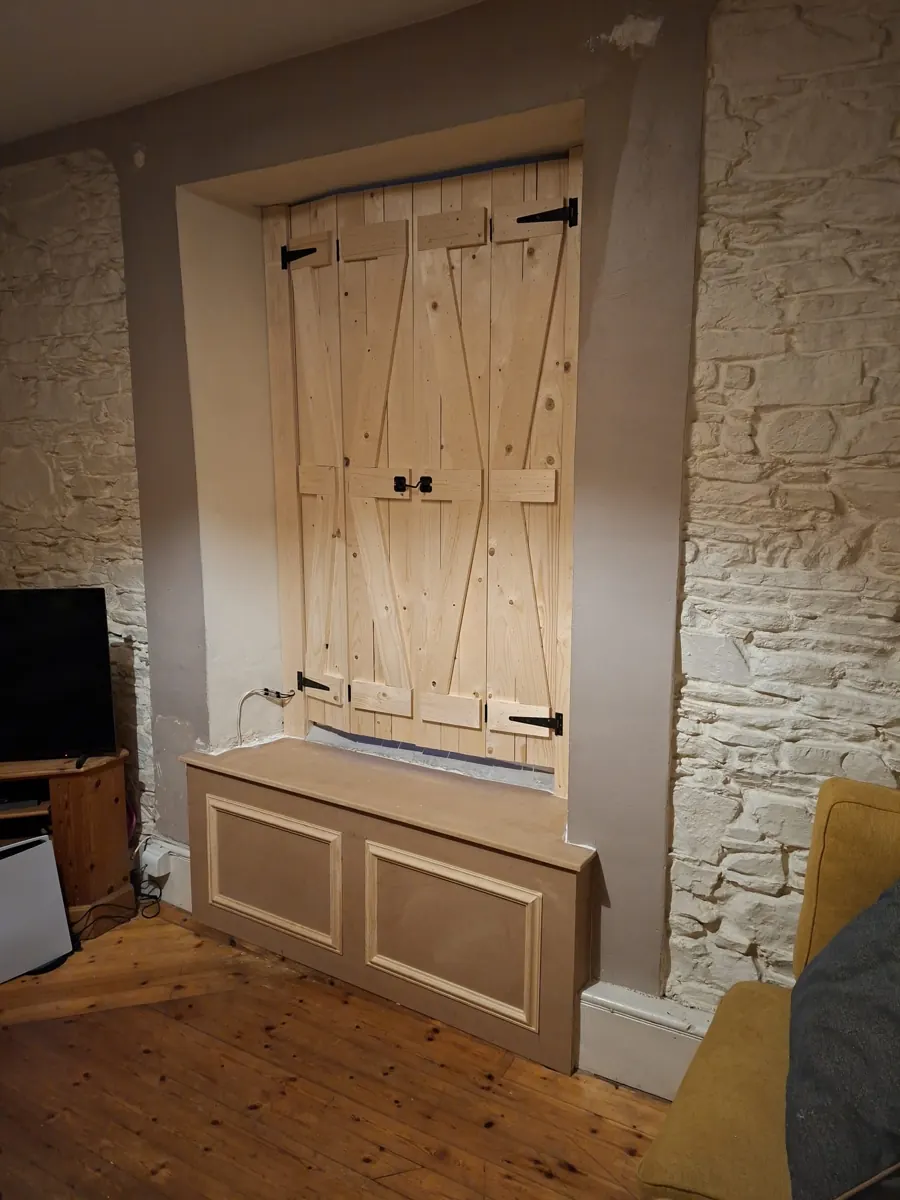 Timber shutters and window-seat storage unit fitted into a wall opening.