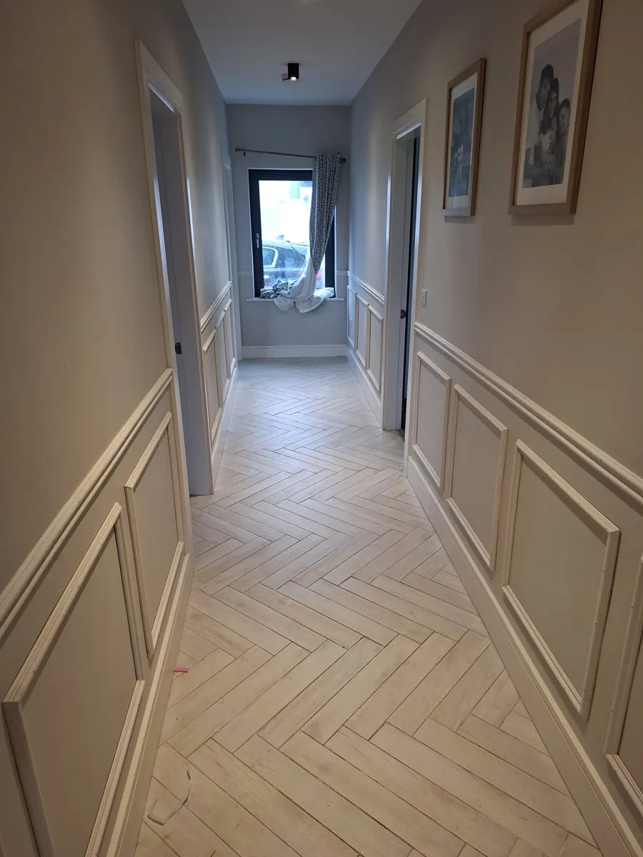 Hallway with decorative wall panelling and herringbone-style flooring.